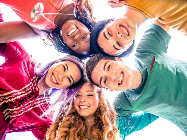 Cinq amis souriants se tenant en cercle.