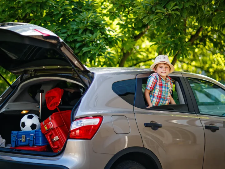 Enfant souriant dans une voiture, valises derrière.