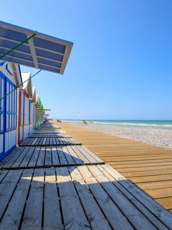 Cabanes colorées sur plage ensoleillée avec promenade en bois.