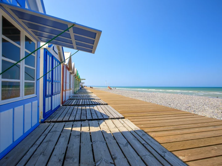 Cabanes colorées sur plage ensoleillée avec promenade en bois.