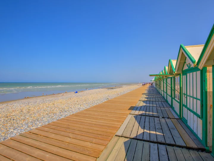 Plage ensoleillée avec cabines en bois, ciel bleu.