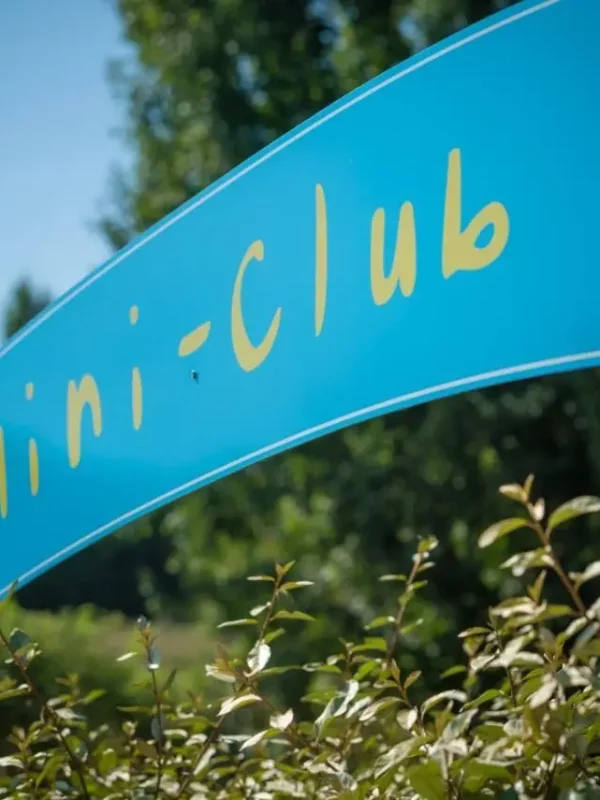 Panneau bleu indiquant Mini-Club parmi les arbres.