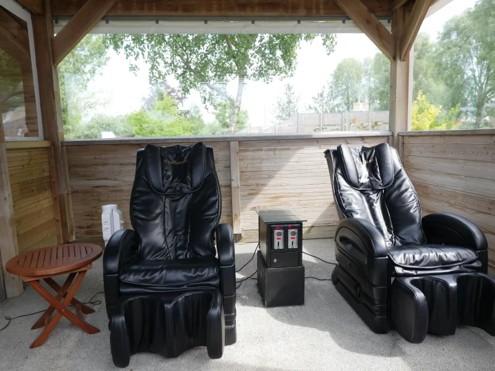 Deux fauteuils massants noirs sous un gazebo en bois.