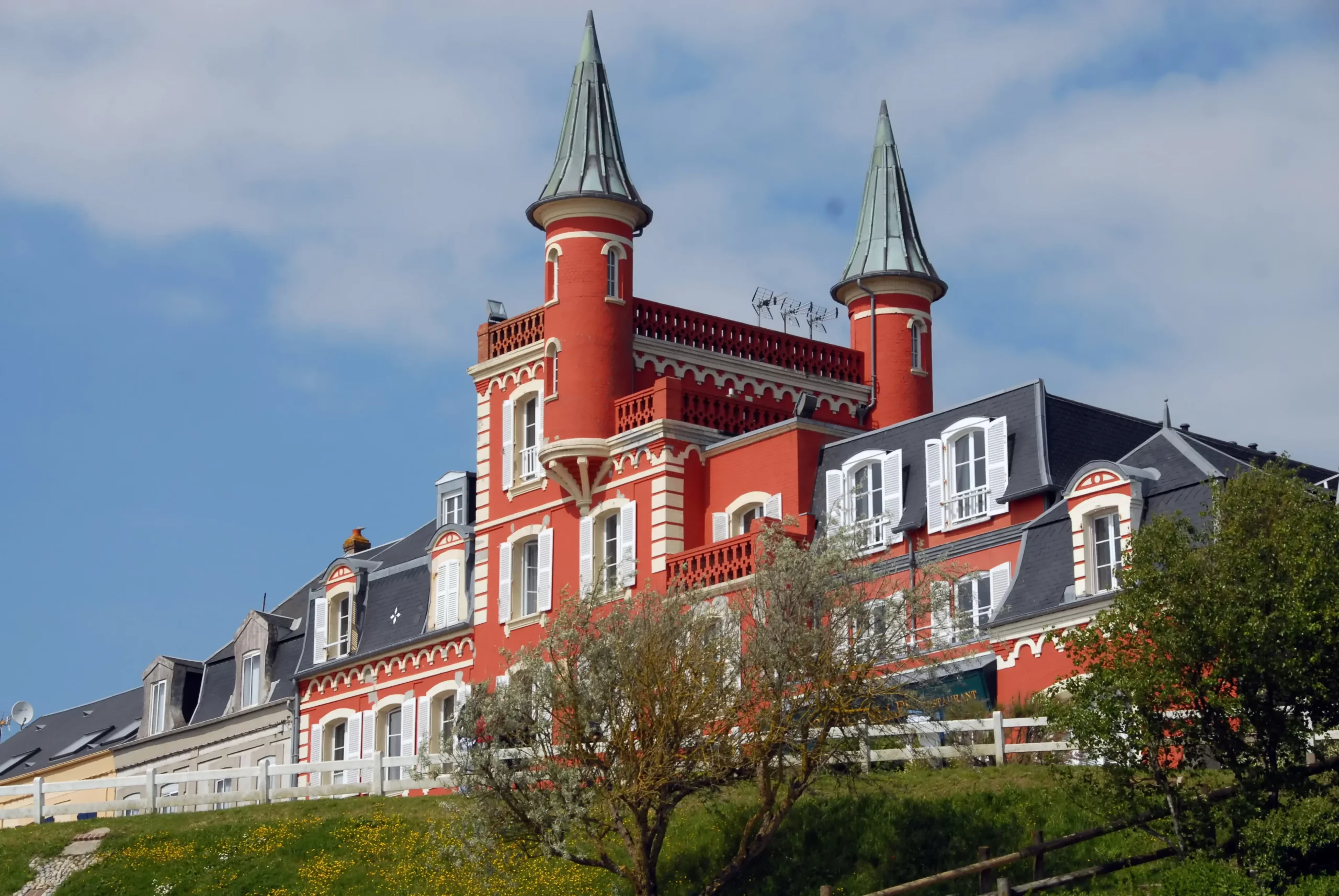 Maison rouge avec tours et fenêtres blanches.
