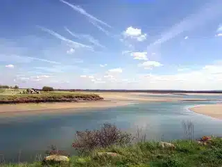Estuaire sableux sous ciel bleu avec nuages blancs.