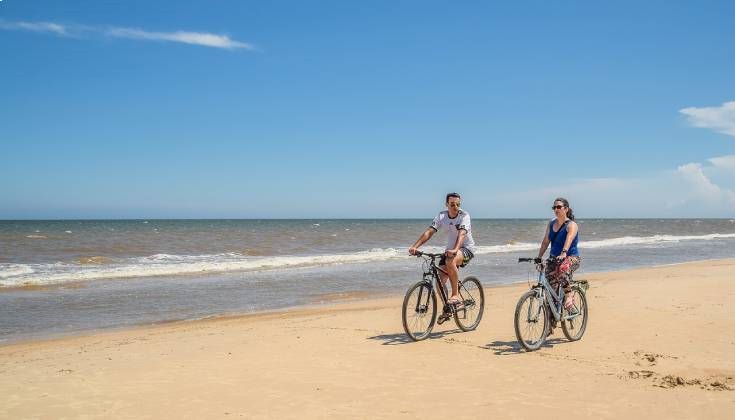 Deux personnes à vélo sur une plage ensoleillée.