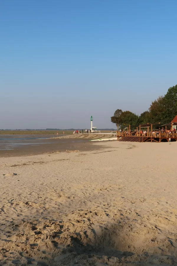 Plage avec maison et phare au loin.